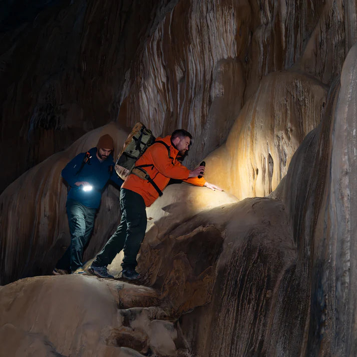 Two people exploring a cave with headlamps in a dark, rocky environment.